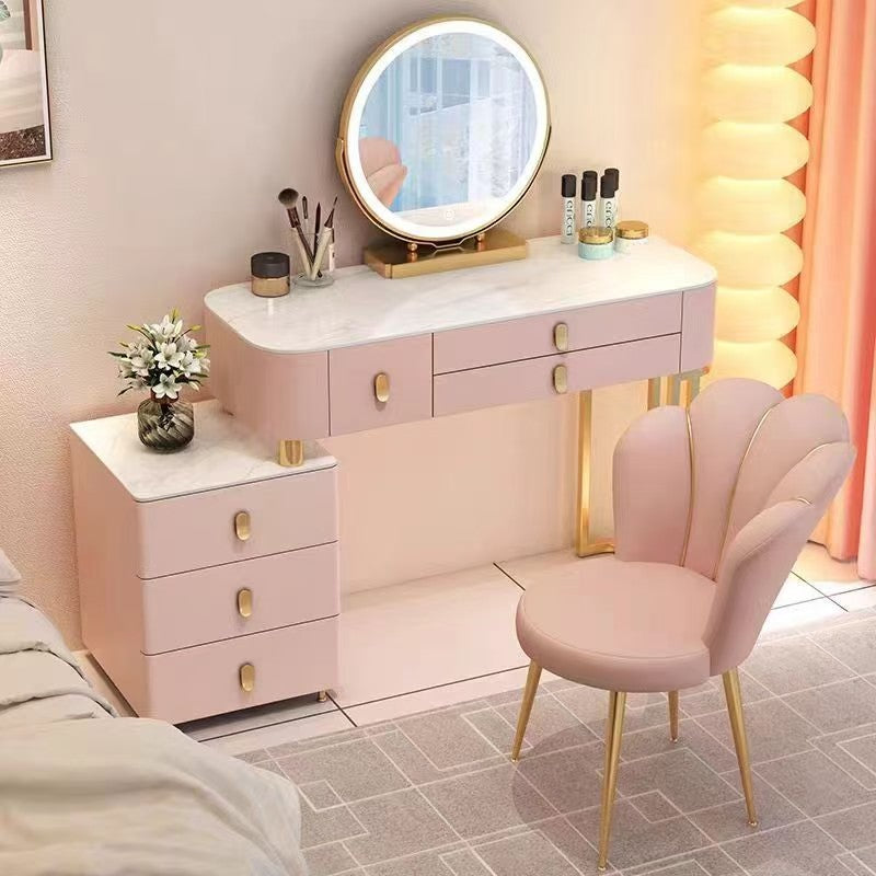 Pink vanity table with round mirror and chair in a room with pink curtains.
