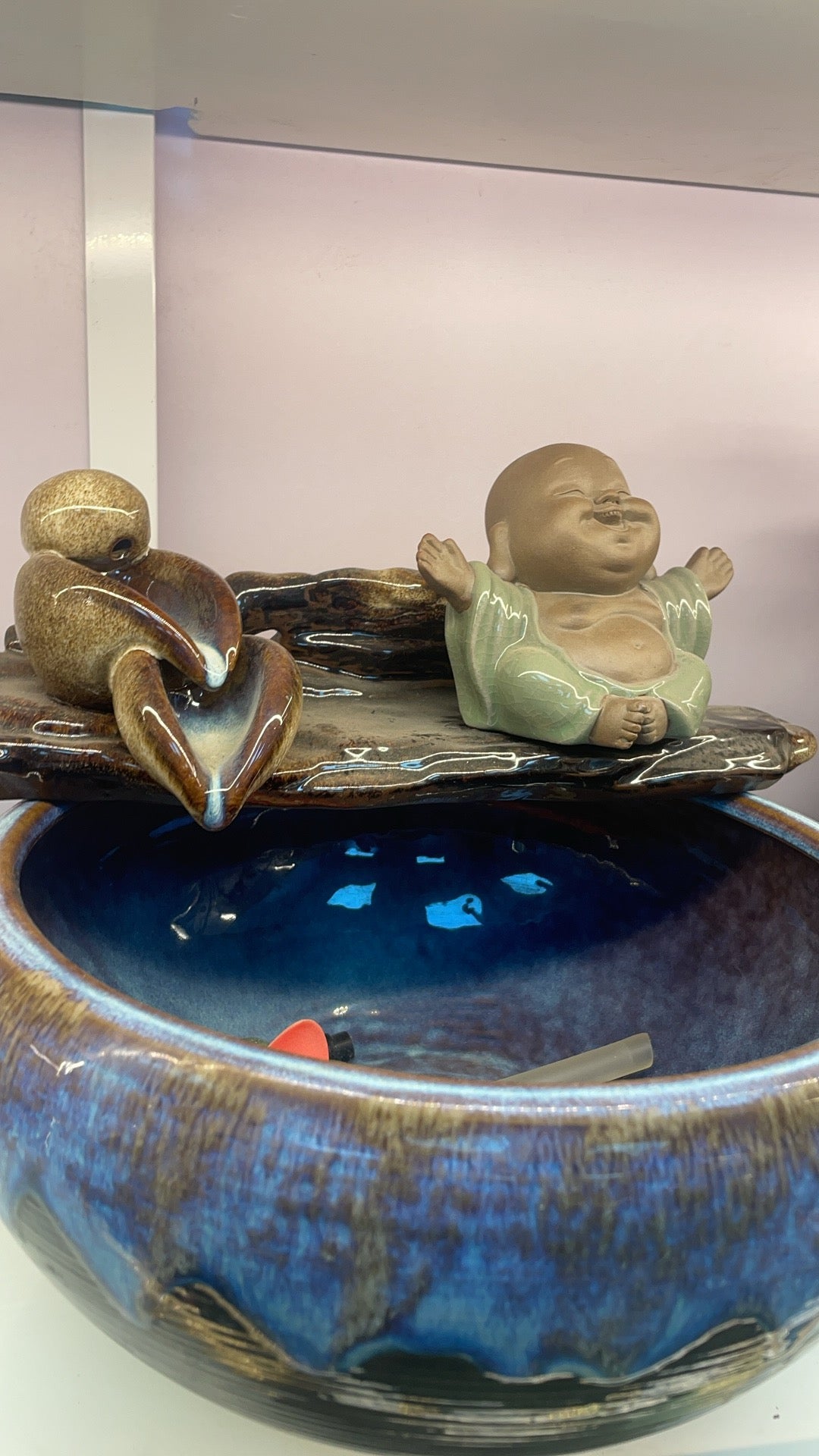 Decorative ceramic piece with a small Buddha figure and a fish on a blue base.