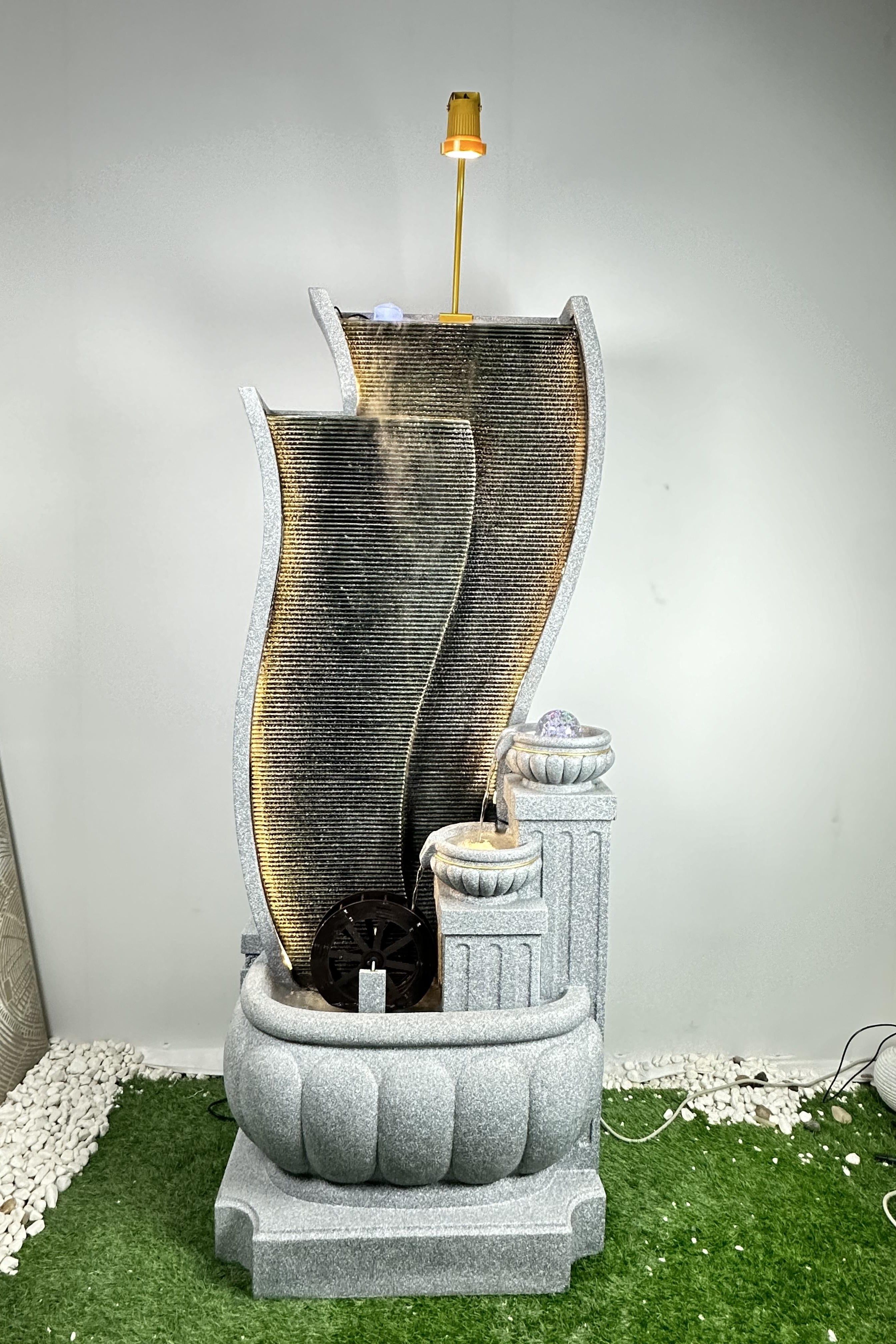 Decorative stone fountain with three curved tiers on a grassy area.